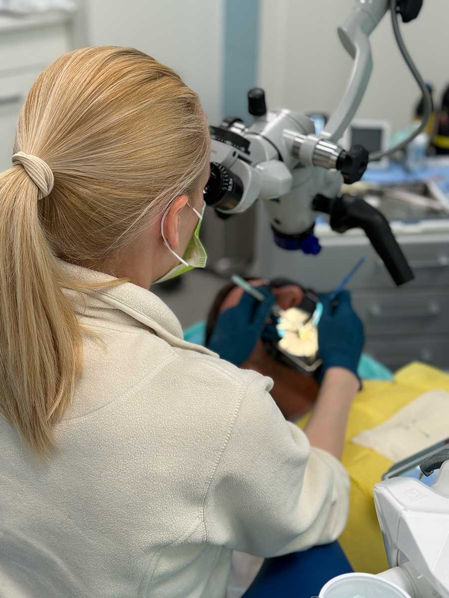 Widok zza pleców lekarki pracującej pod mikroskopem zabiegowym